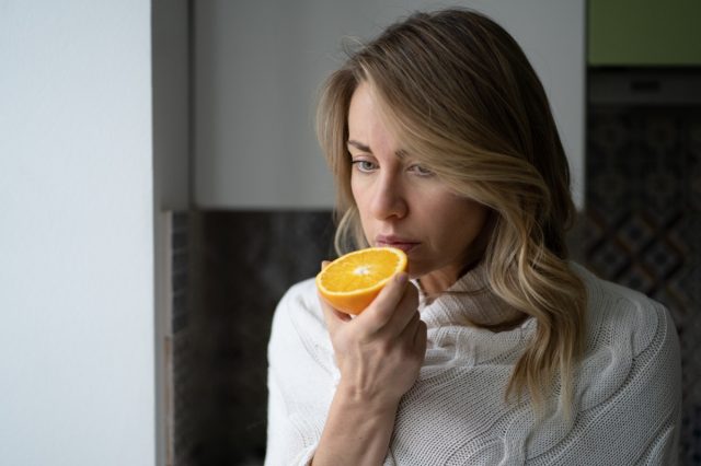 Une femme essayant de sentir une demi-orange fraîche présente des symptômes de Covid-19