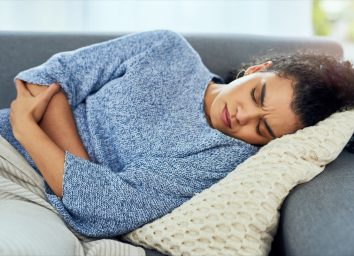 Woman experiencing stomach pain on the sofa at home