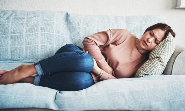 Woman lying on sofa and suffering from stomach pain.