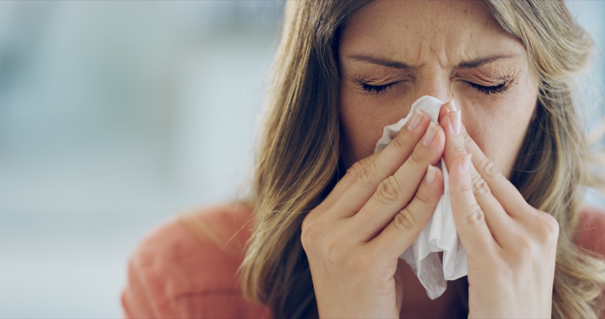 Woman feeling ill and blowing her nose with a tissue at home.