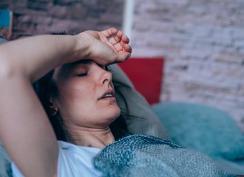 Sick young woman lying in the bed covered with blanket