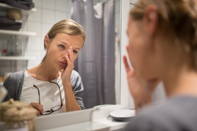 Groggy, young woman yawning in front of her bathroom mirror