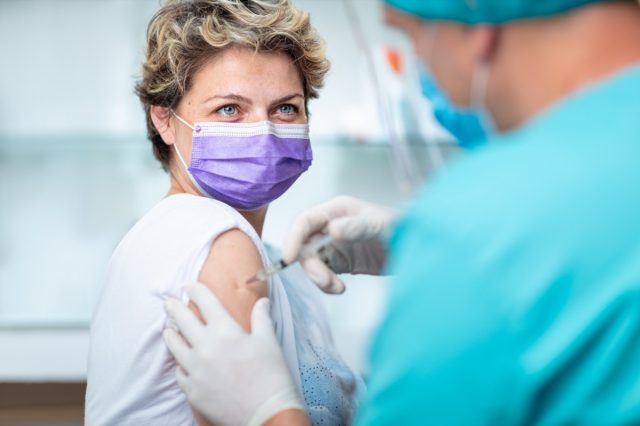 Female patient smiling behind face mask and with her eyes out, while getting flu shot