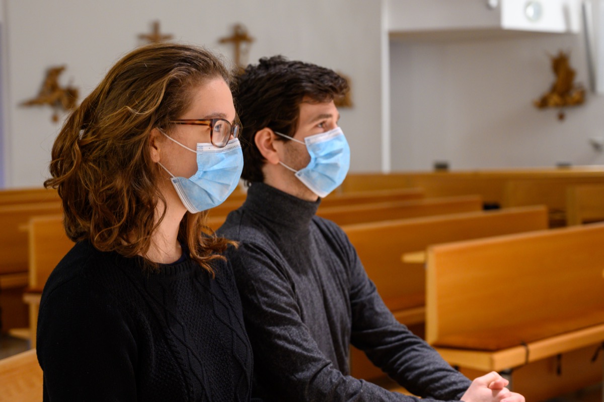A young couple in face masks praying in a church during the COVID-19 pandemic.