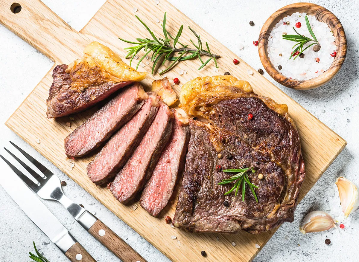 sliced steak on cutting board with fork and knife