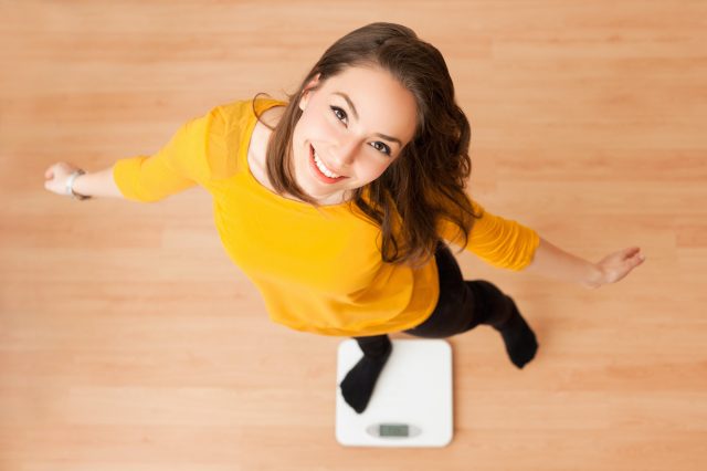 Female standing on scale, satisfied with weight loss