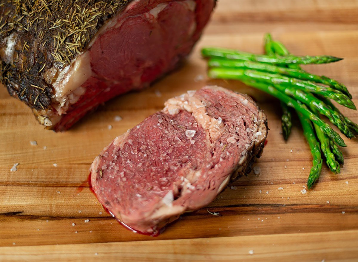 slice of prime rib on cutting board with asparagus and flaky salt