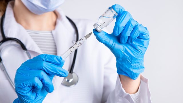 Doctor holding syringe, medical injection in hand with glove.