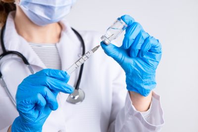 Doctor holding syringe, medical injection in hand with glove.