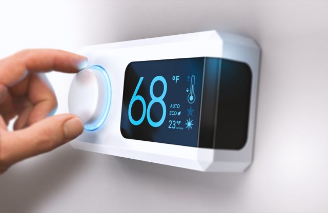 Hand turn a home thermostat knob to set the temperature in energy saving mode