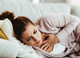 Woman having chest pain and coughing while lying down on sofa at home.