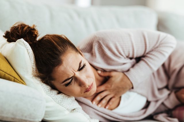 Woman having chest pain and coughing while lying on the sofa at home.