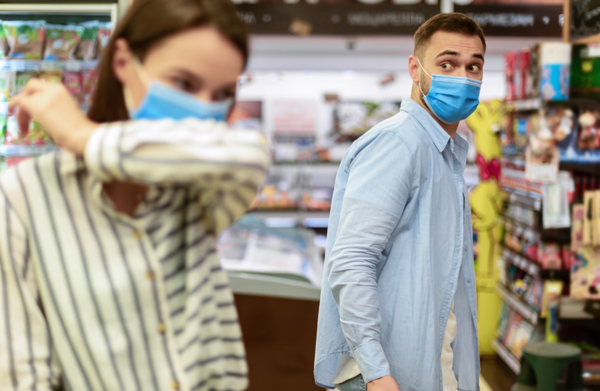 Woman coughing in her elbow in grocery store.