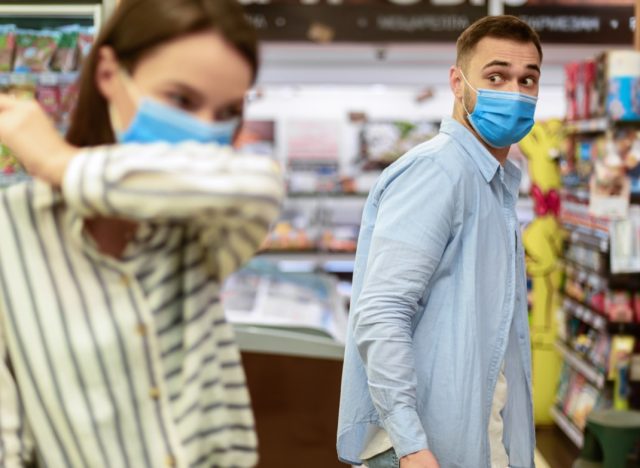 Woman coughing in her elbow in grocery store.