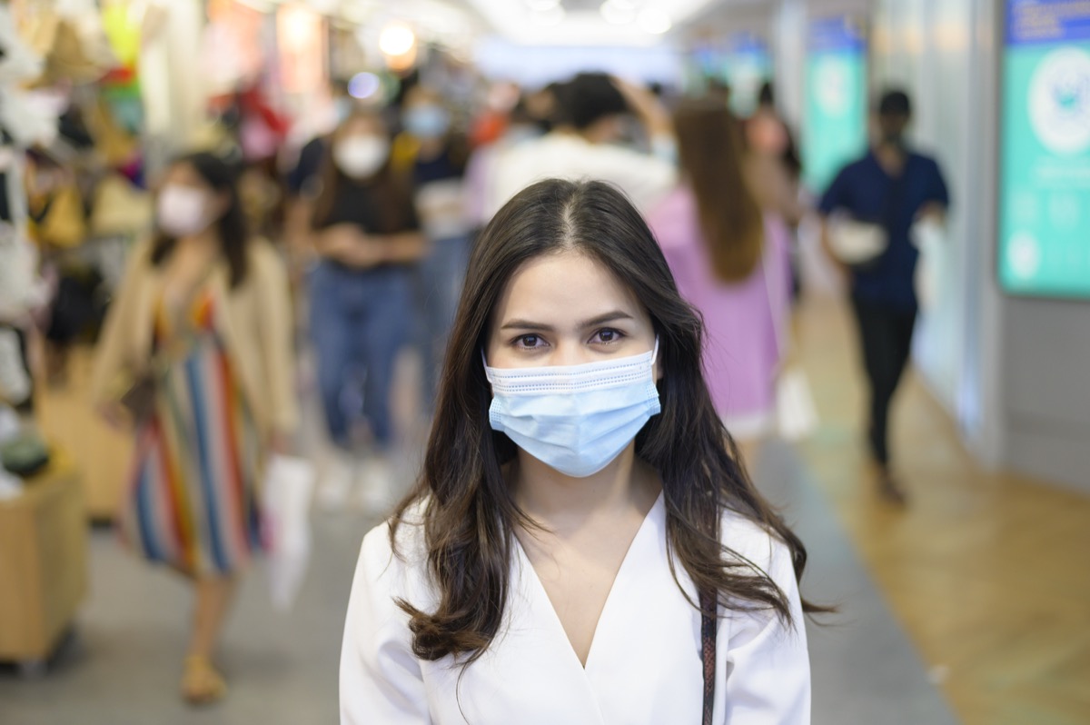 A woman is wearing protective mask on Street with Crowded people while covid-19 pandemic.