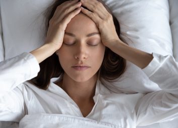 Depressed woman suffering from headache, lying in bed