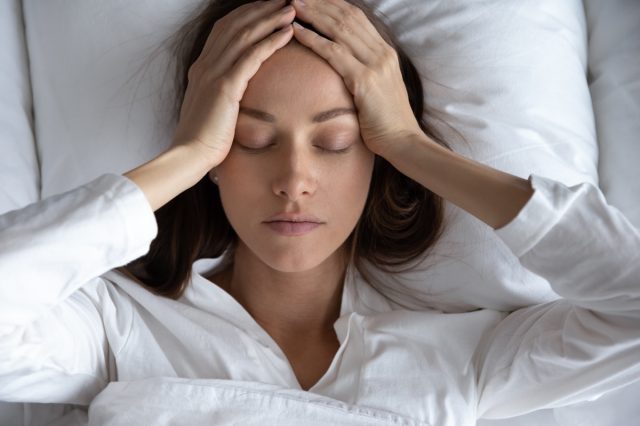 Depressed woman suffering from headache, lying in bed