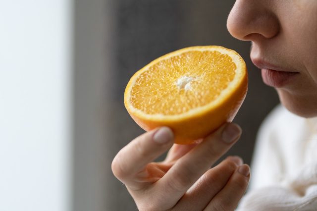 Sick woman trying to sense smell of half fresh orange, has symptoms of Covid-19, corona virus infection - loss of smell and taste
