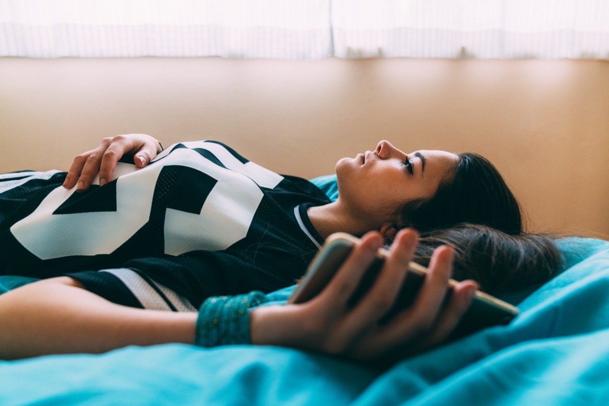 woman laying on bed with a phone in her hand.