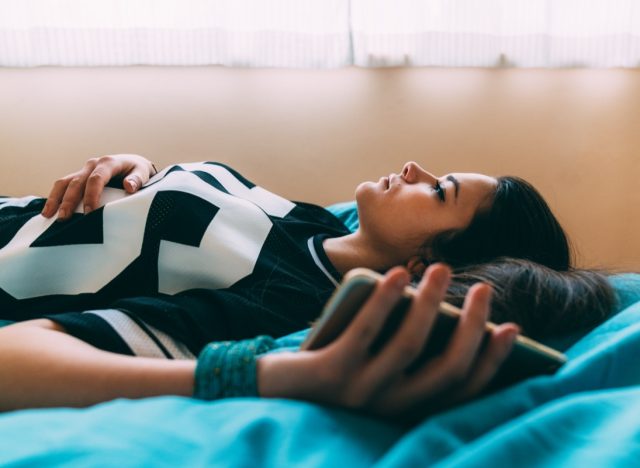 woman laying on bed with a phone in her hand.