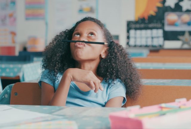 Young girl looking bored while playing at a school desk.