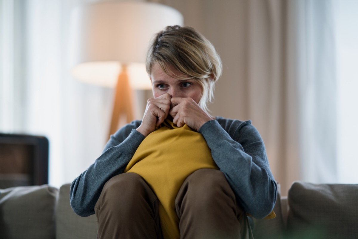 Woman with tablet indoors on sofa at home feeling stressed, mental health concept.