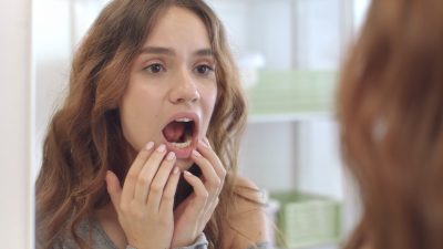 Young woman with opened mouth checking teeth in mirror in home bath room.