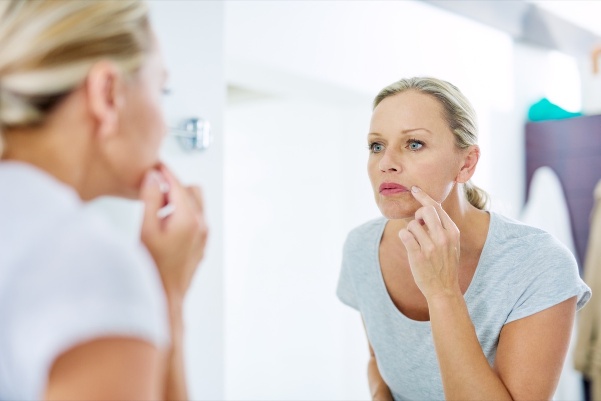 Mature woman inspecting her skin in front of the bathroom mirror.