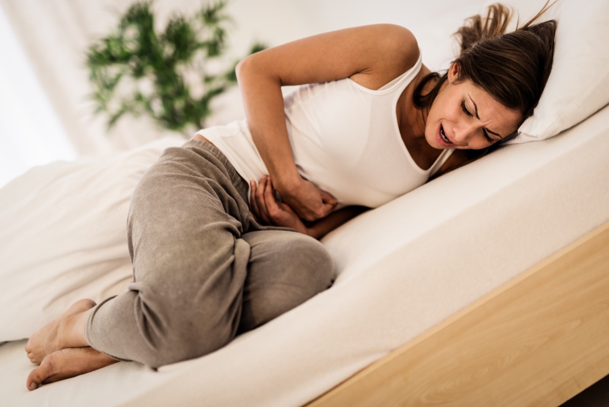 Woman lying on bed and holding hands on her stomach.