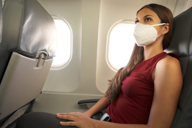 Eine Frau sitzt in einem Flugzeug und trägt eine KN95 FFP2-Schutzmaske