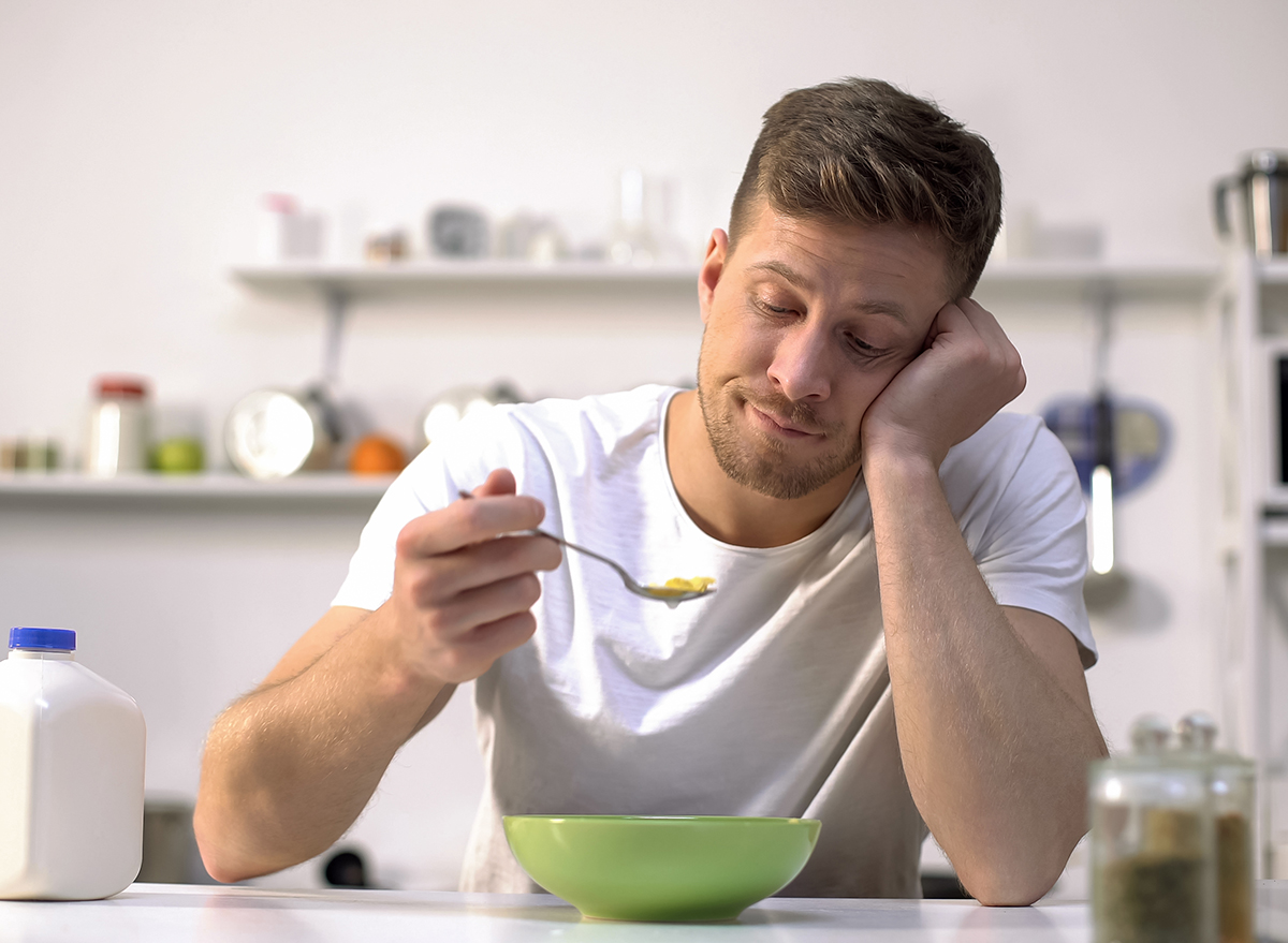 bored man eating bowl of cereal in kitchen