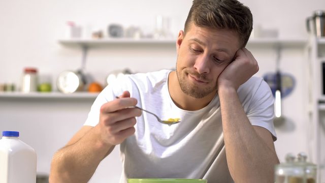 bored man eating bowl of cereal in kitchen
