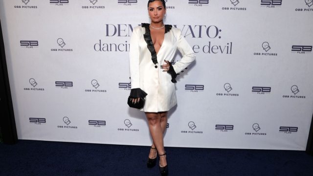 demi lovato in white dress with black trim on step-and-repeat for dancing with the devil miniseries