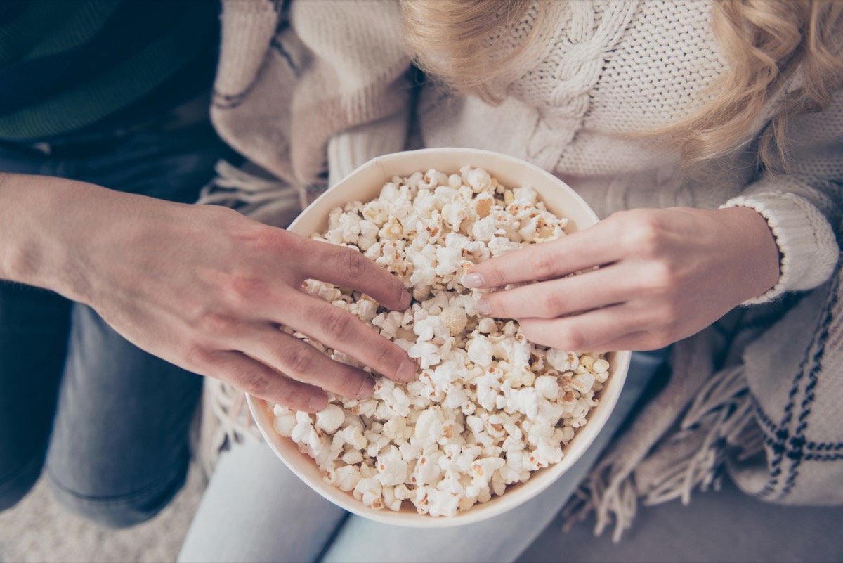 two people in sweaters putting their hands into a bowl of popcorn