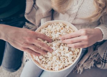 two people in sweaters putting their hands into a bowl of popcorn