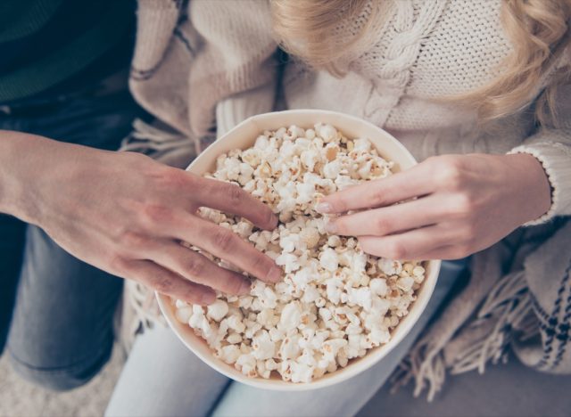 two people in sweaters putting their hands into a bowl of popcorn