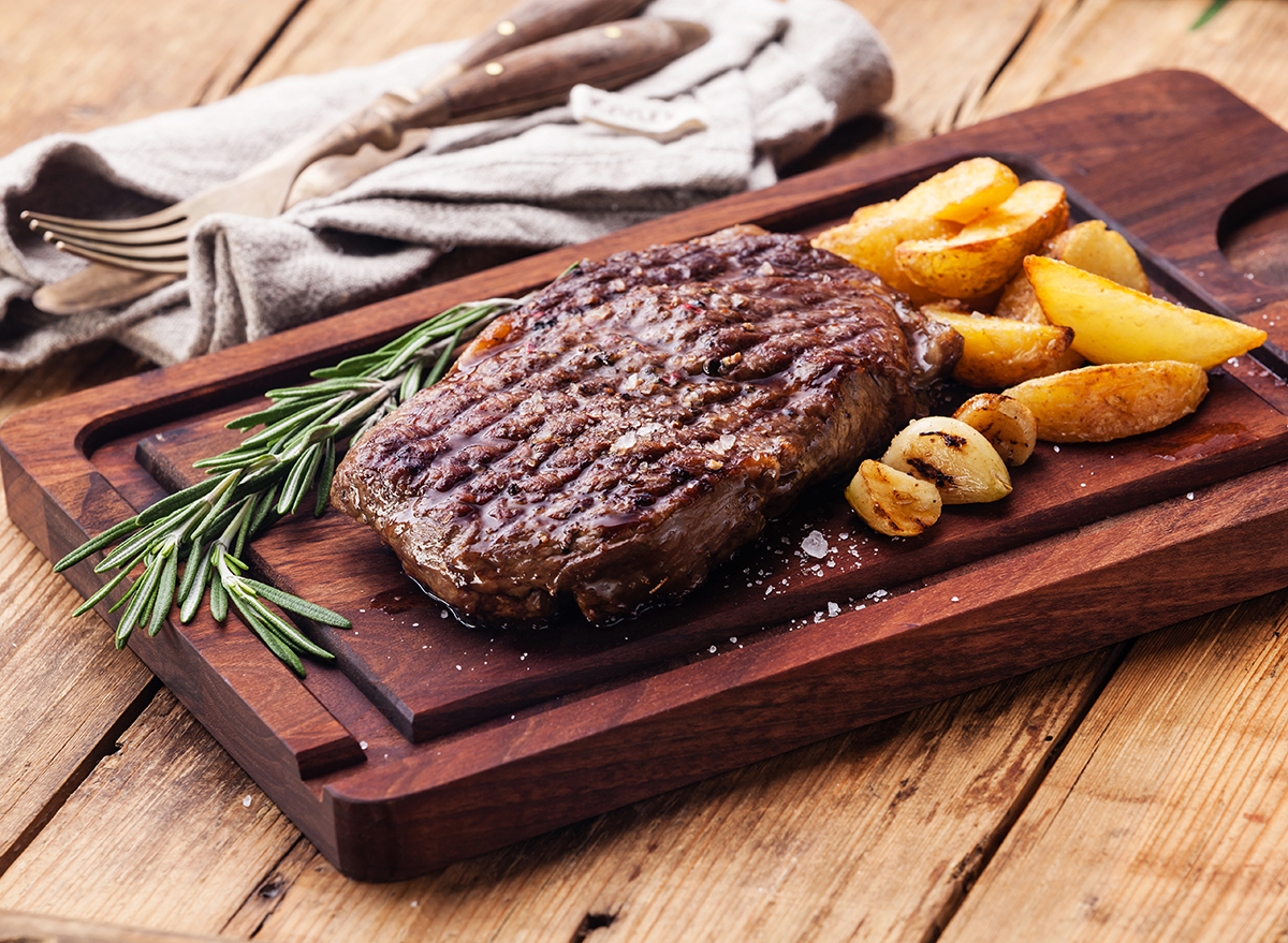 ribeye steak dinner with potatoes on wood board