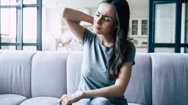 Woman in pain touching her back while sitting on the couch.