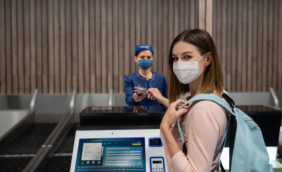 Traveling woman doing the check-in at the airport wearing a face mask.