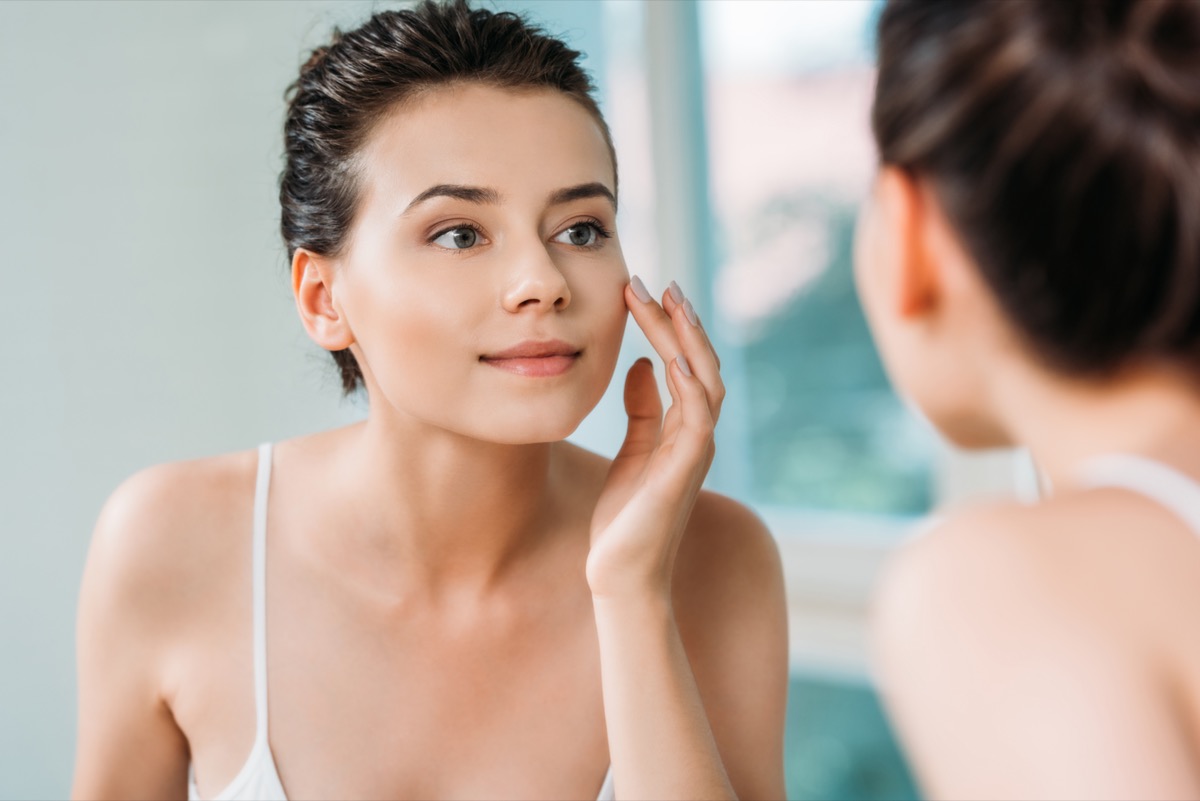 Frau berühren Gesicht und Blick auf Spiegel im Badezimmer