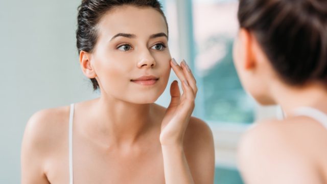 Woman touching face and looking at mirror in bathroom