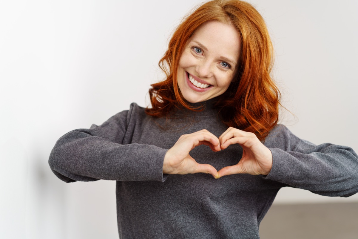 Woman making a heart gesture with her fingers in front of her chest.
