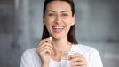 happy woman holds pill glass of water looks at camera