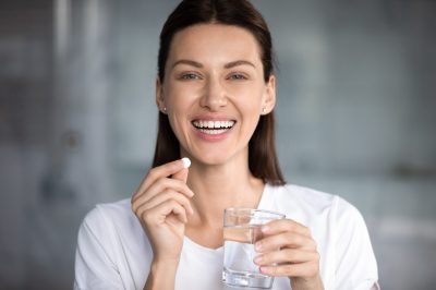 happy woman holds pill glass of water looks at camera