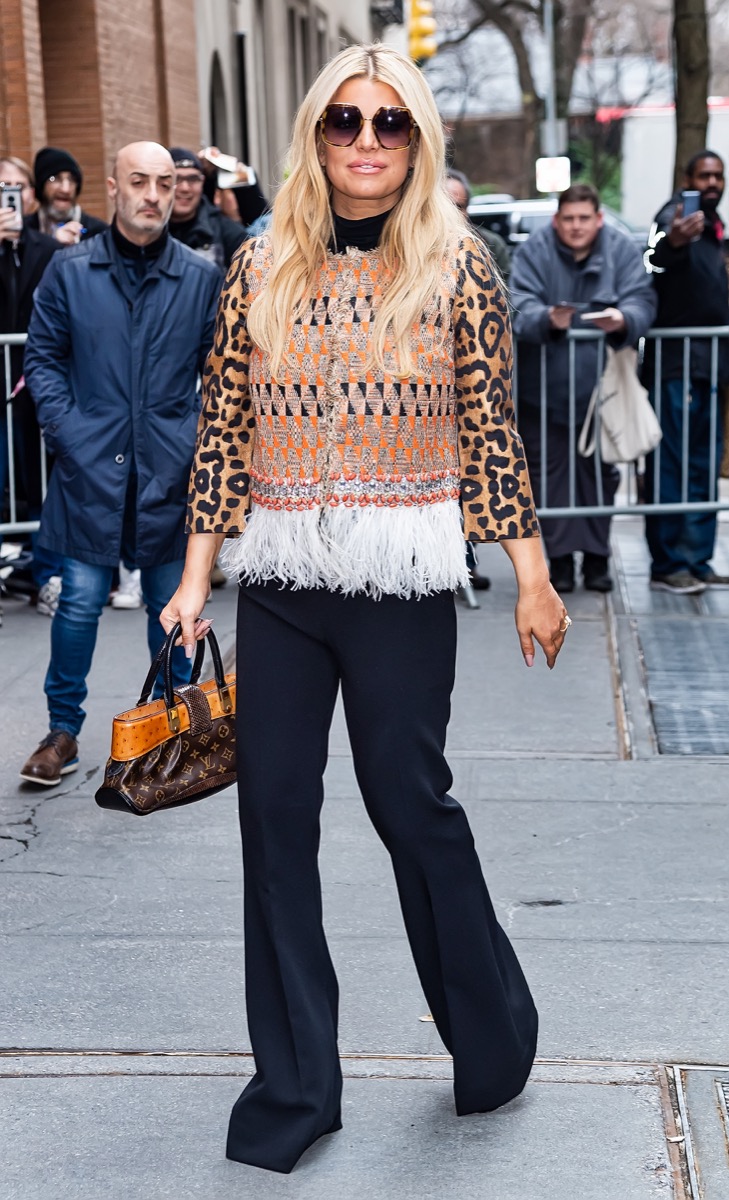 jessica simpson con pantalones negros, camiseta de leopardo y chaleco con flecos con bolso louis vuitton en la calle