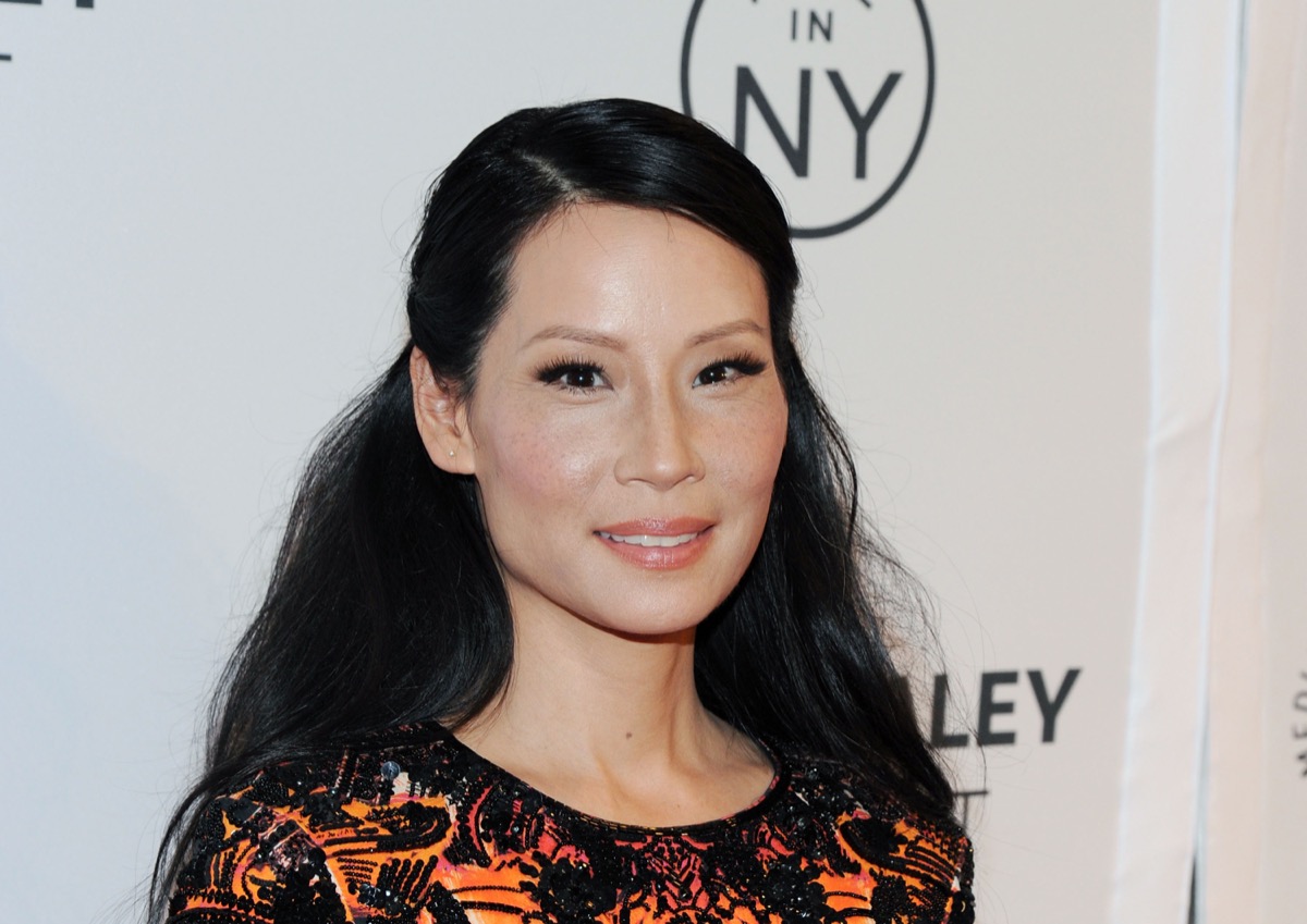 lucy liu with her hair half up, half down in front of white step-and-repeat