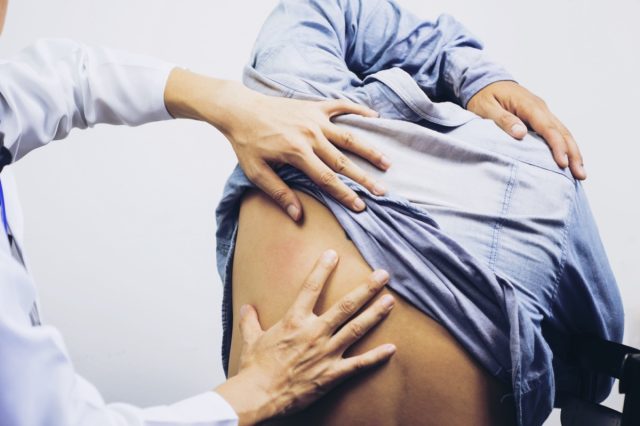 A male physiotherapist examining mans back in the medical office.