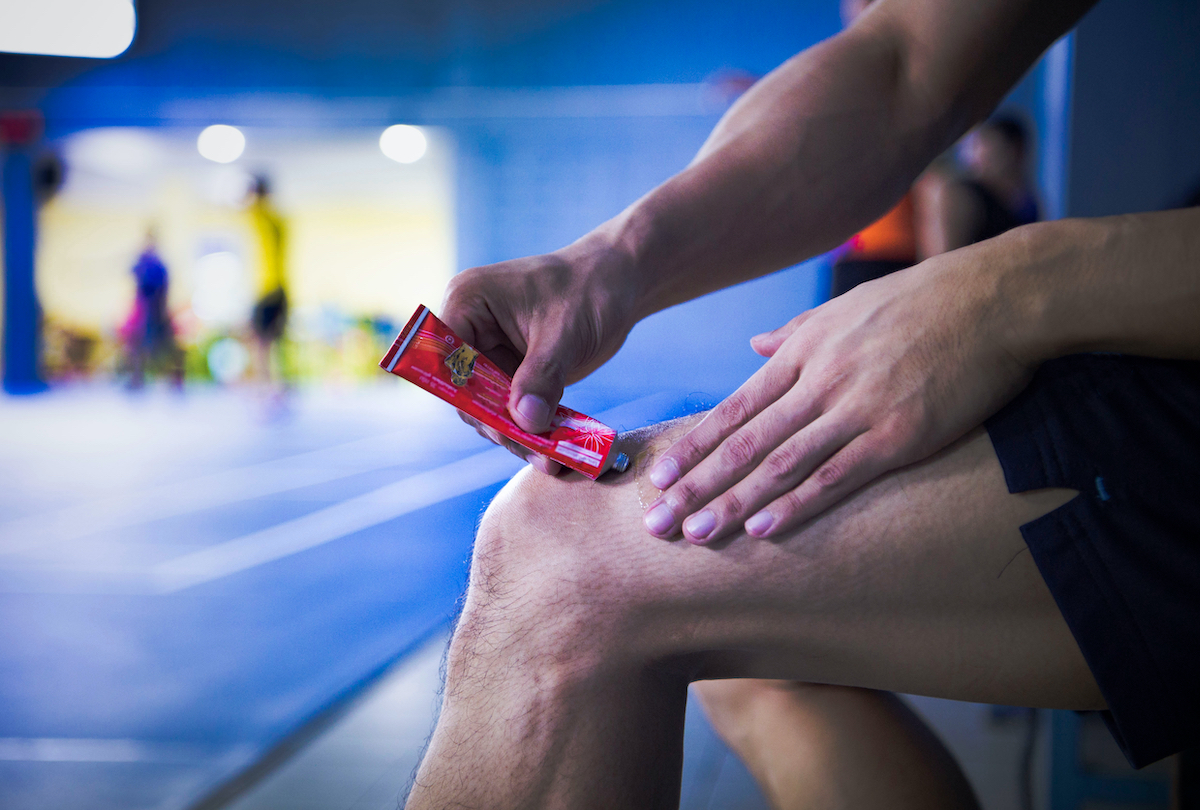 A fitness man applying ointment cream (lotion) onto his knee to relieve the pain or injury