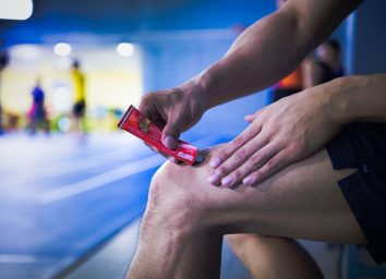 A fitness man applying ointment cream (lotion) onto his knee to relieve the pain or injury