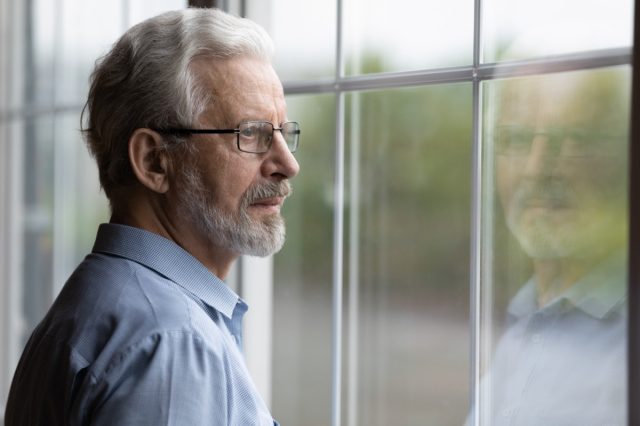 Senior man in eyeglasses looking in distance out of window